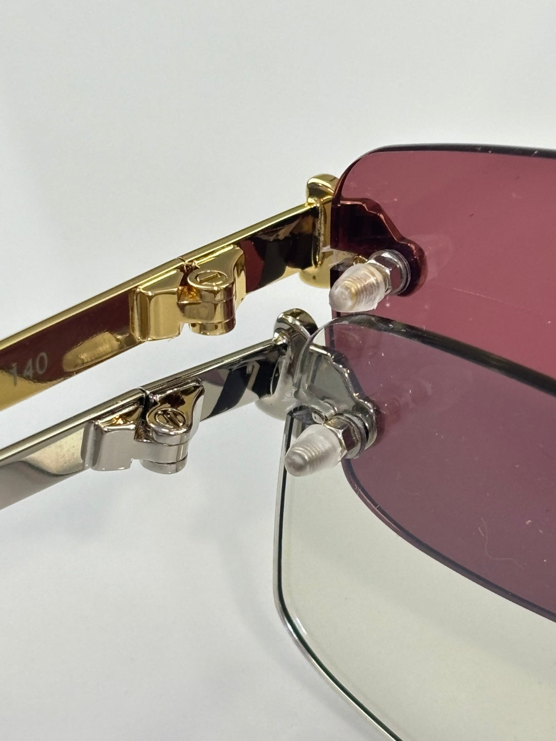 Gold-trim eyeglass hinge with maroon-tinted lens and clear frame hardware