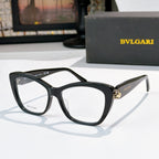 Black cat-eye eyeglasses with clear lenses and gold logo detail at the temple hinge