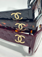 Eyeglasses close-up: glossy dark maroon temples with gold Chanel emblem details.