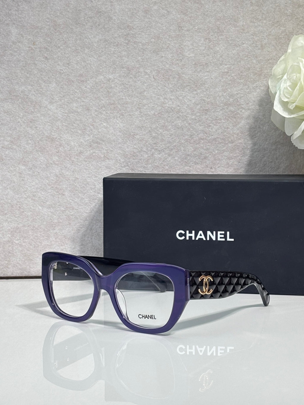 Eyeglasses with blue frames and patterned temple, featuring a gold Chanel logo.