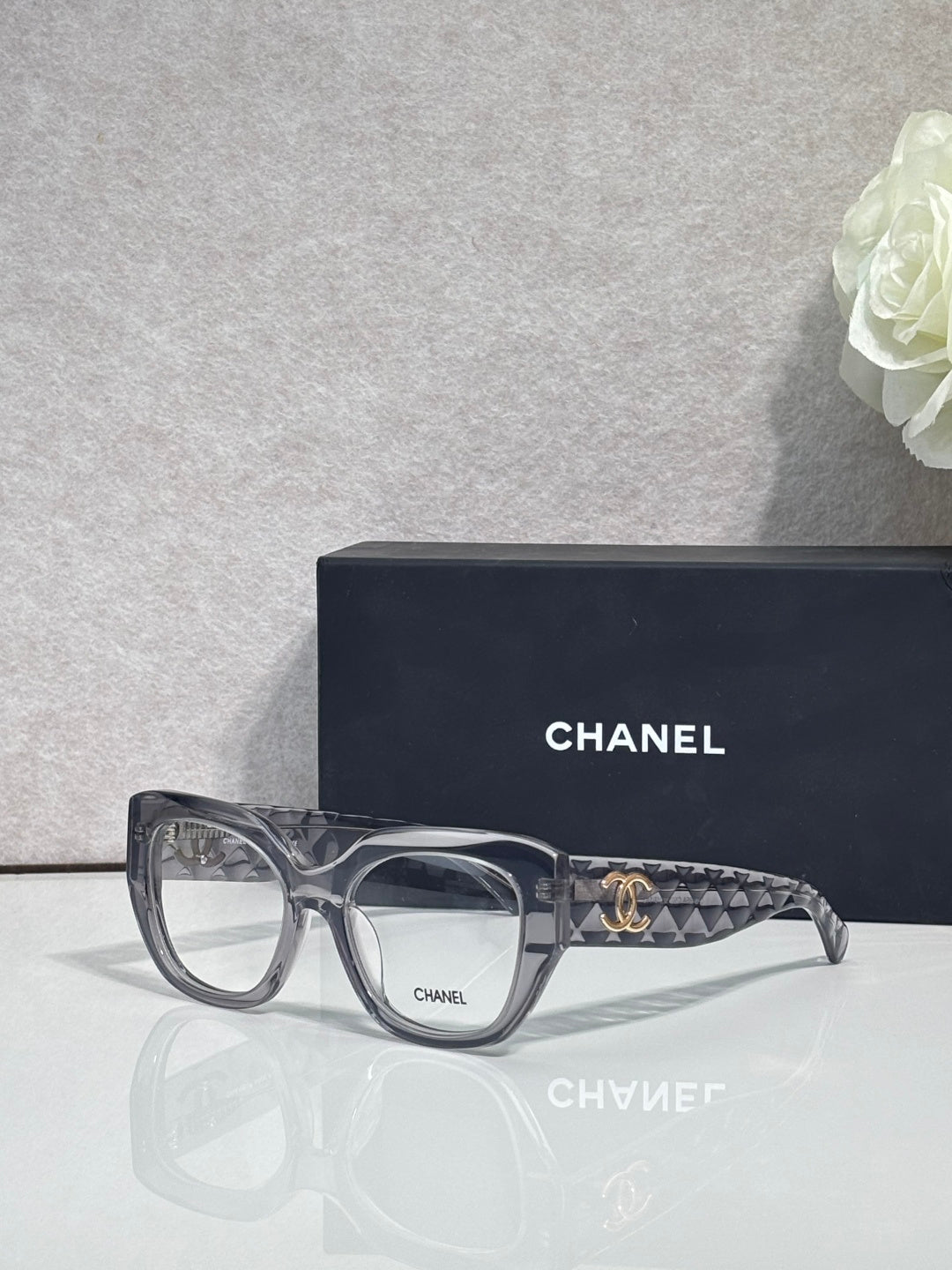 Eyeglasses with gray frames, dark tortoiseshell temple, and gold Chanel logo detail.