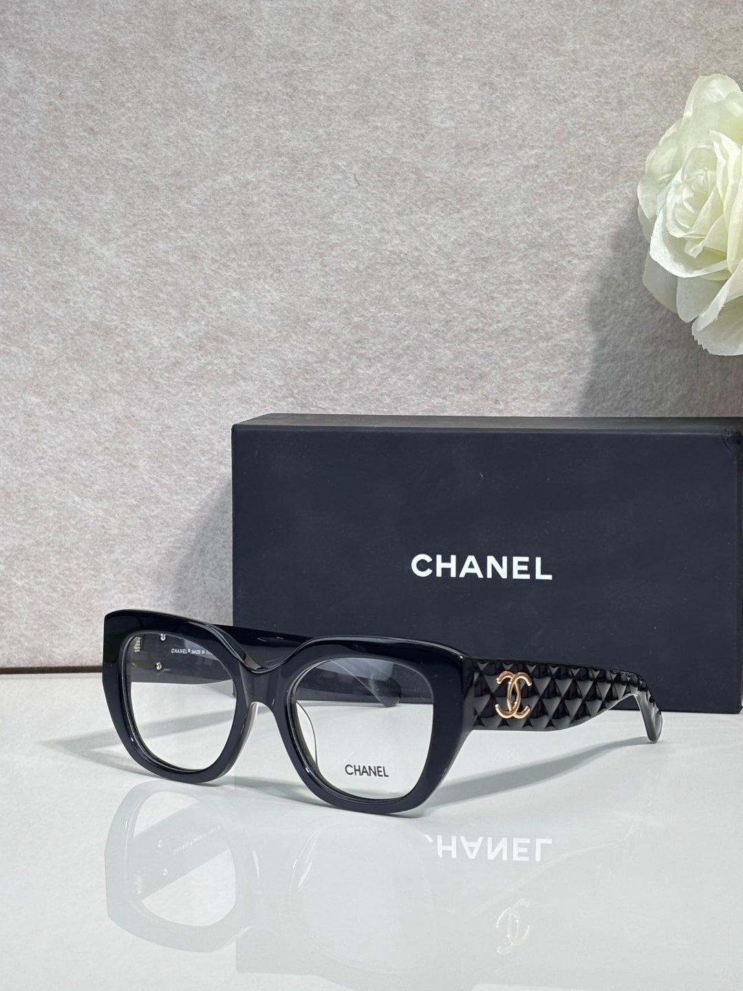 Eyeglasses with black frames and patterned temple, featuring a gold Chanel logo.