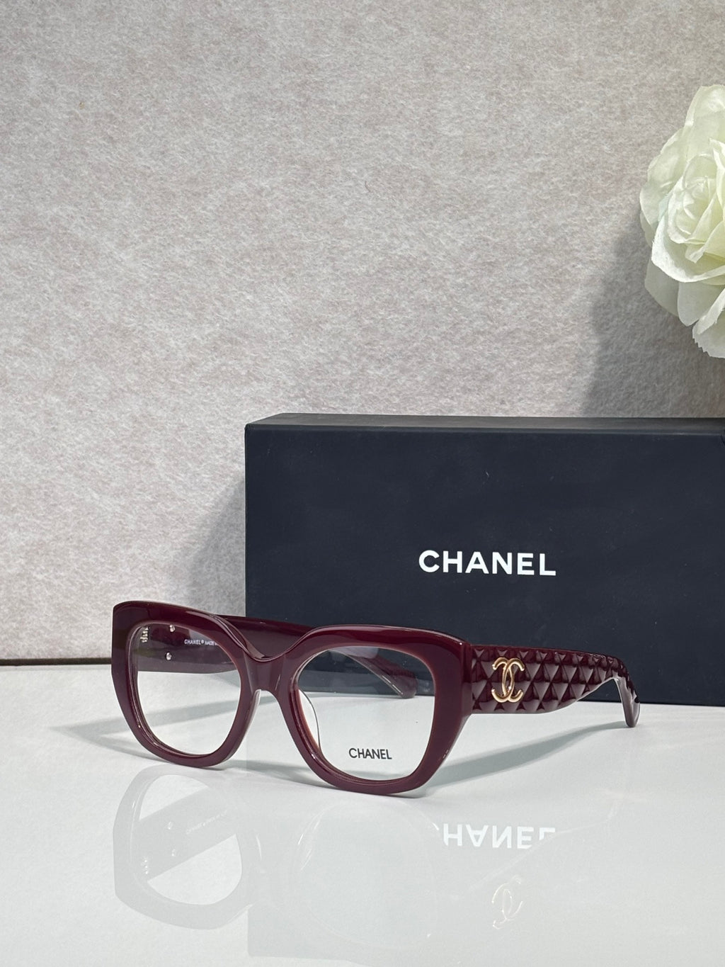 Eyeglasses with burgundy frames and patterned temple, featuring a gold Chanel logo.