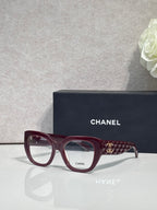 Eyeglasses with burgundy frames and patterned temple, featuring a gold Chanel logo.