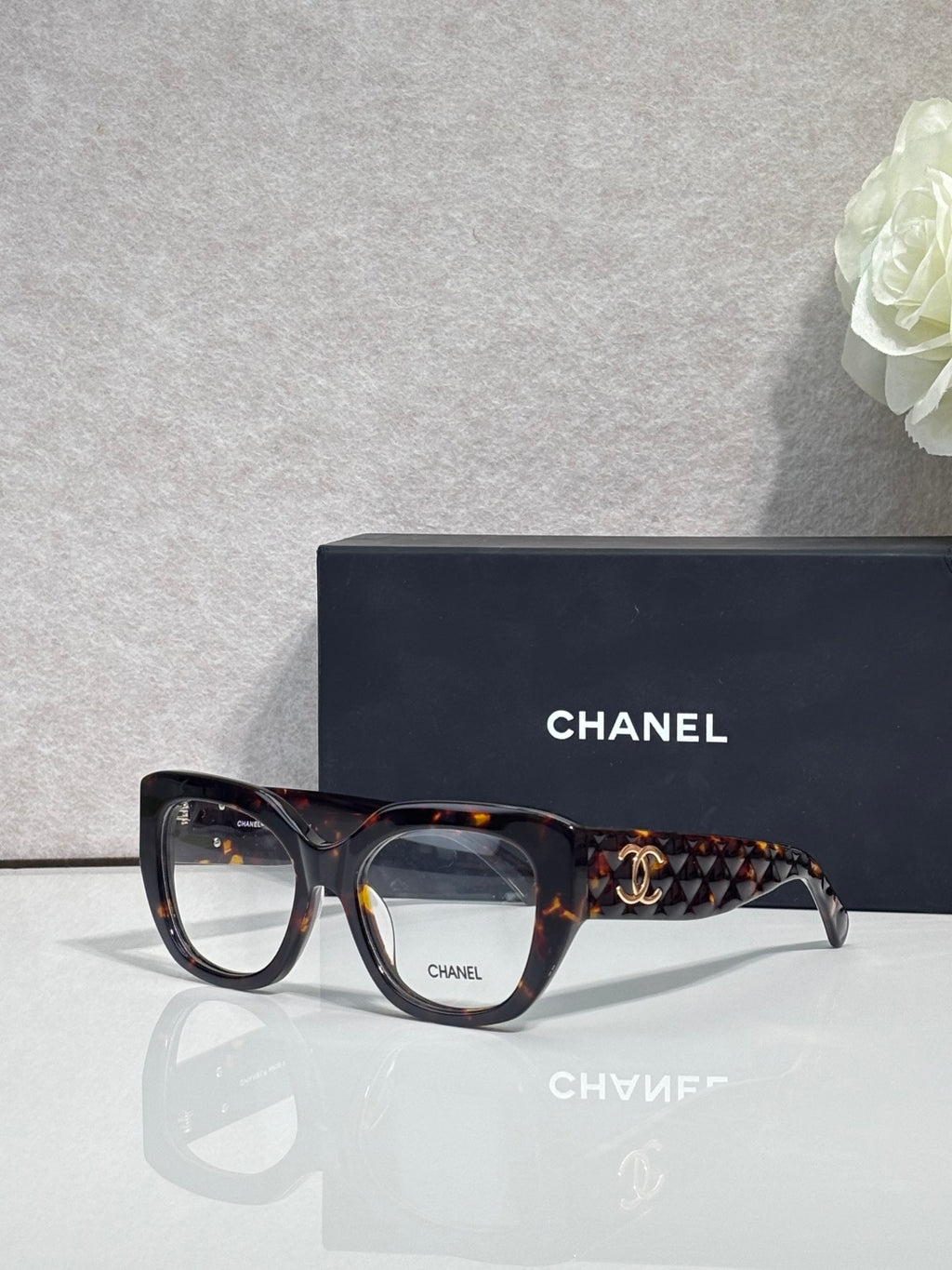 Eyeglasses with dark tortoiseshell frames, patterned temple, and gold Chanel logo.