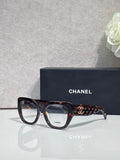 Eyeglasses with dark tortoiseshell frames, patterned temple, and gold Chanel logo.
