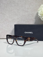 Eyeglasses with dark tortoiseshell frames, patterned temple, and gold Chanel logo.