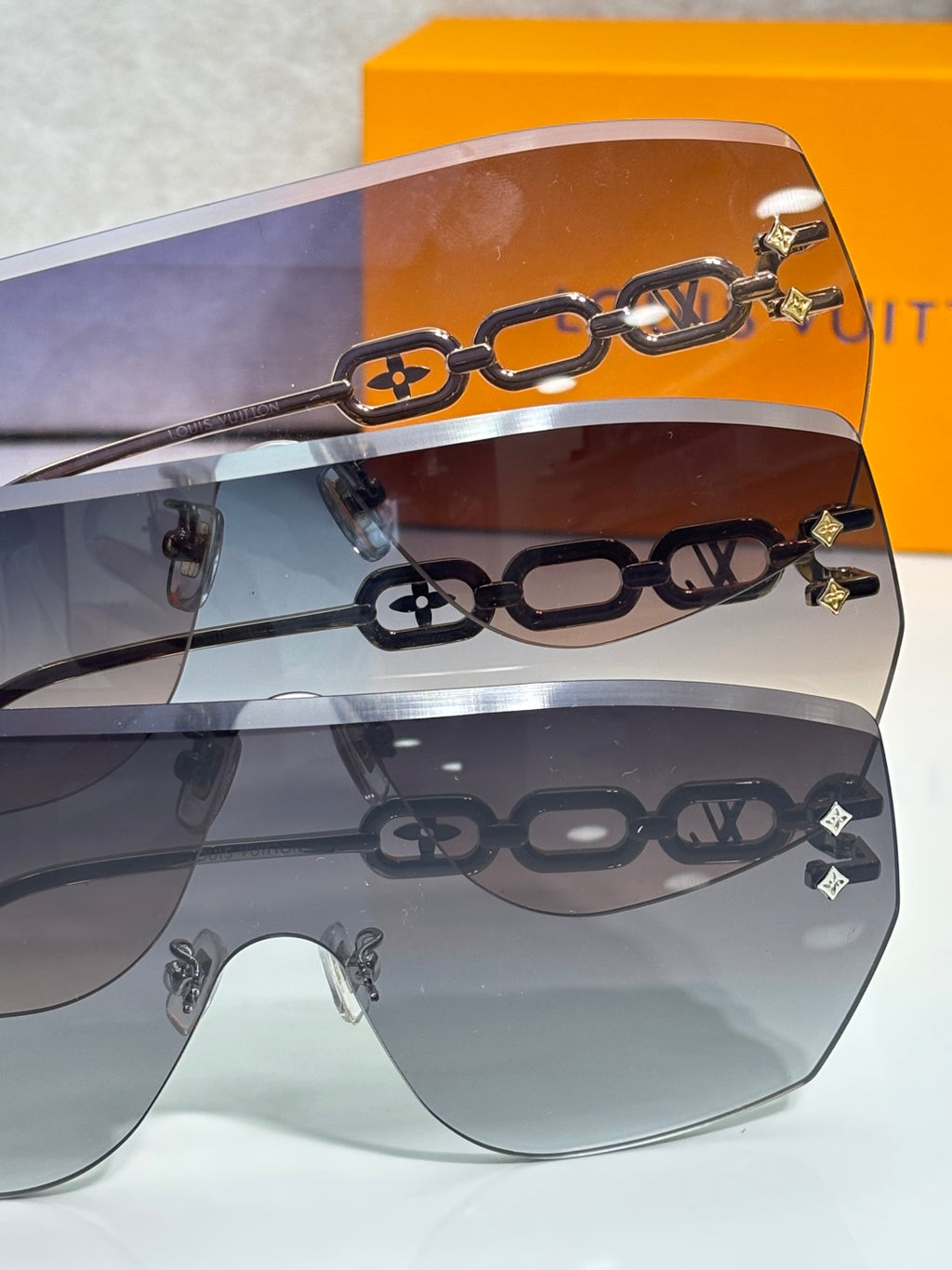 Louis Vuitton sunglasses close-up with gold chain motif over gradient lenses
