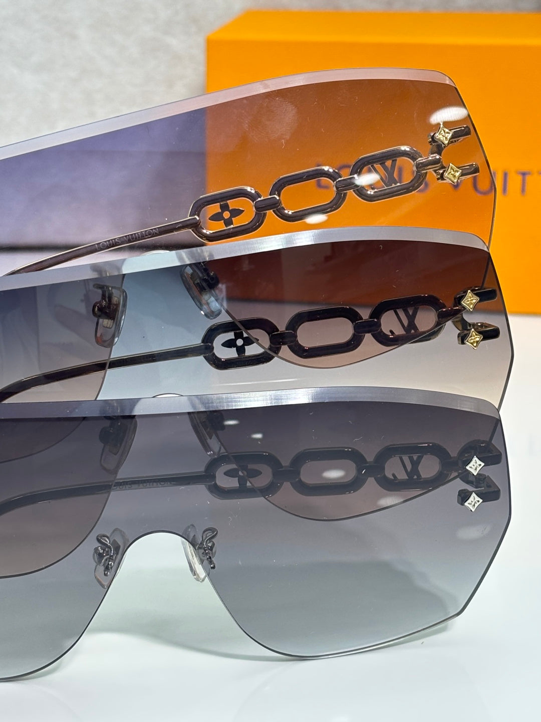 Louis Vuitton sunglasses close-up with gold chain motif over gradient lenses