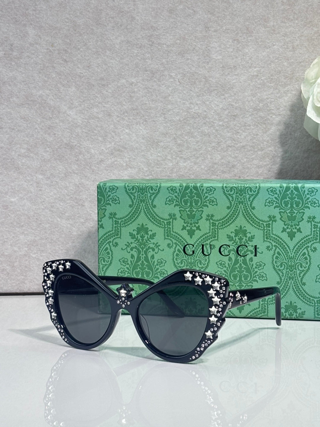 Gucci glasses with dark navy cat-eye frames, rhinestone star embellishments, dark lenses.