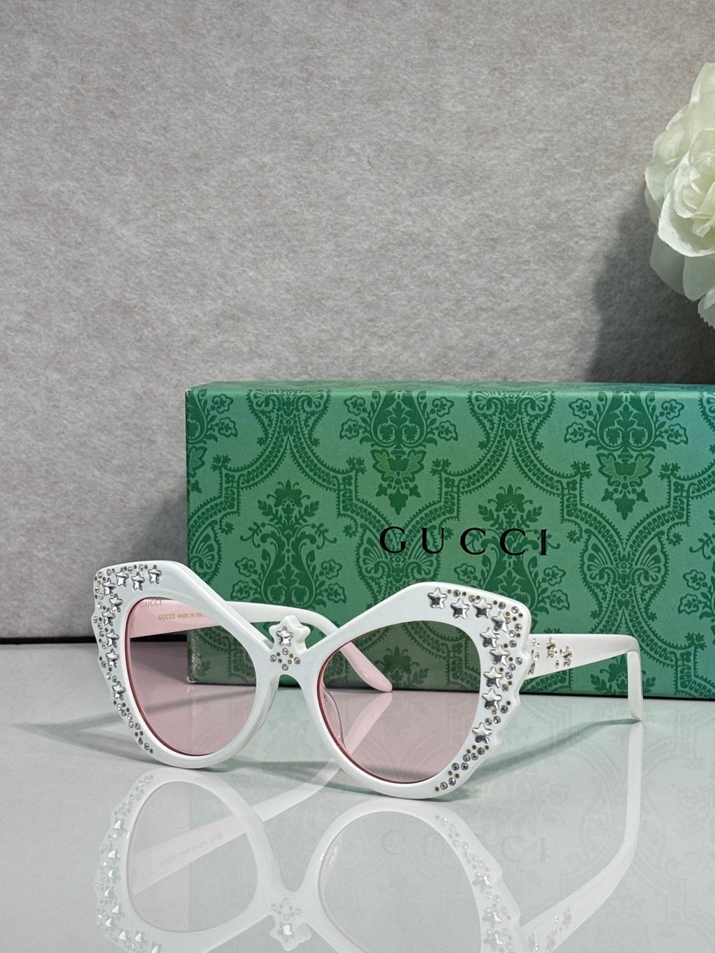 Gucci glasses with white cat-eye frames, rhinestone star detailing, pink-tinted lenses.
