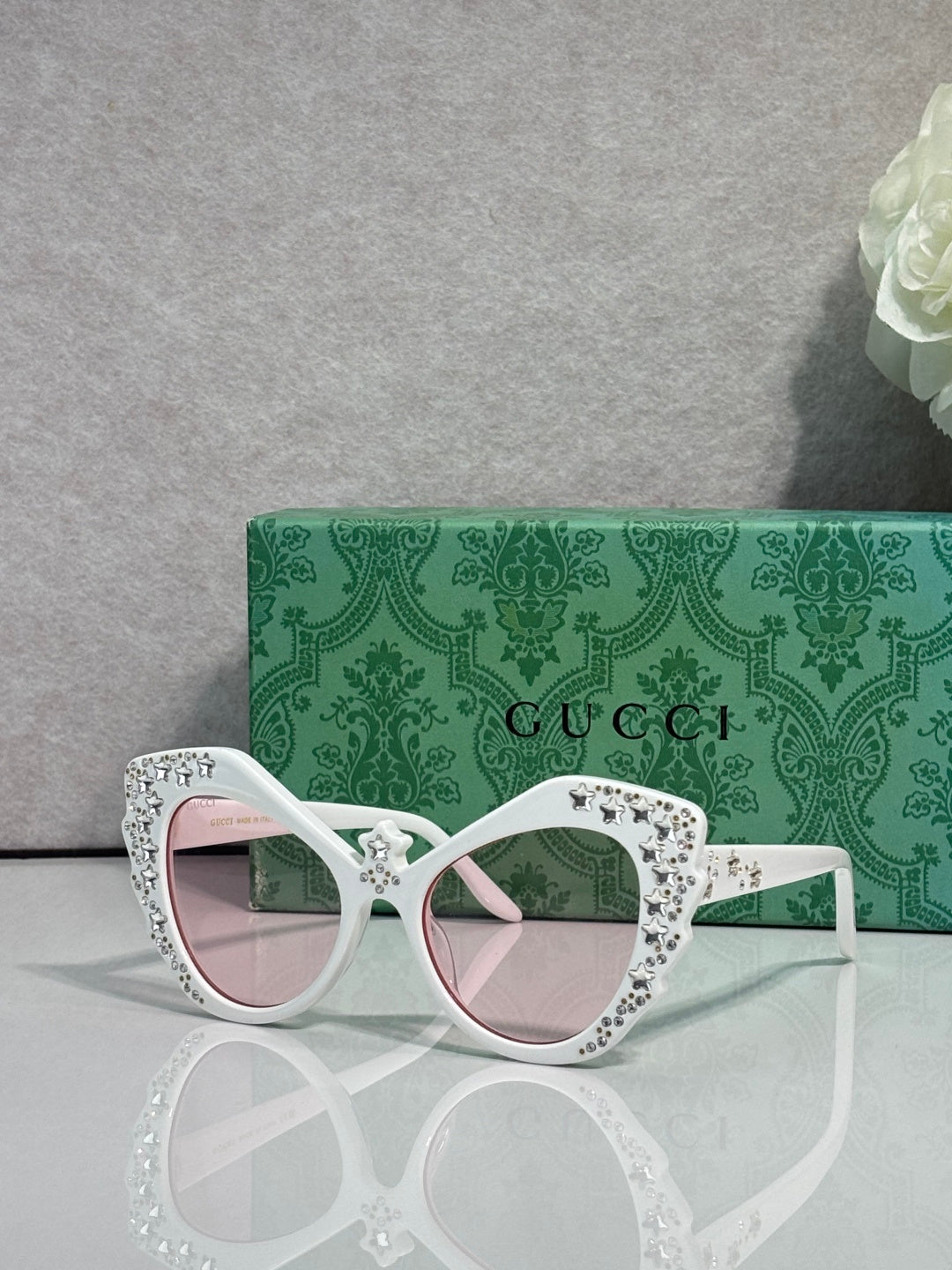 Gucci glasses with white cat-eye frames, rhinestone star detailing, pink-tinted lenses.