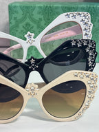 Gucci glasses with white cat-eye frames, rhinestone stars, and mixed dark and pink lenses.