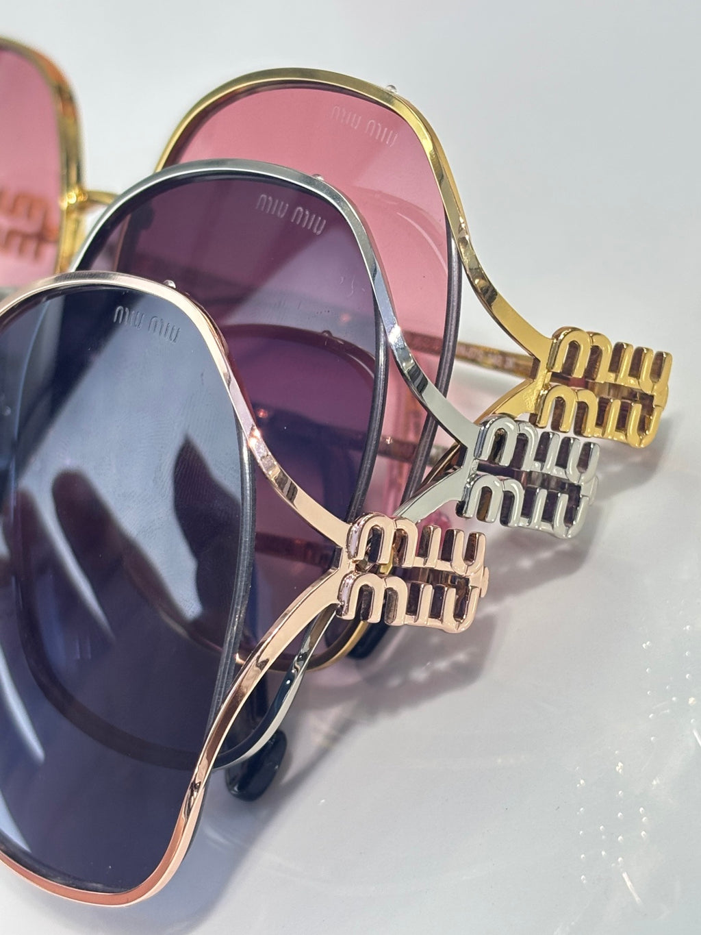 MiuMiu sunglasses close-up: purple and blue gradient lenses, gold engraved temples