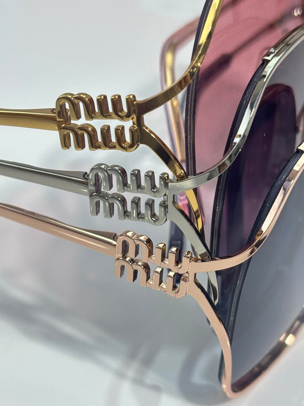 MiuMiu sunglasses close-up: gold bridge and temples with engraved MiuMiu detail