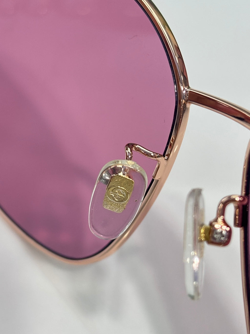 Sunglass lens with rose-pink tint and gold-tone frame detail