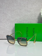 Square sunglasses with dark navy/black frame and blue-tinted lenses, gold metal accents.