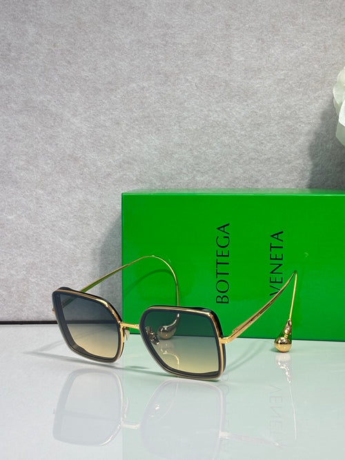 Square sunglasses with dark navy/black frame and blue-tinted lenses, gold metal accents.