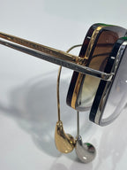 Side close-up of sunglasses with gold bar detailing and dark navy acetate frames.