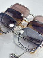 Overlapping square sunglasses with gold frames and tinted lenses in brown, pink, and blue.
