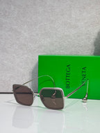 Square sunglasses with dark brown frame and dark brown-tinted lenses, gold metal accents.