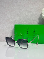 Square sunglasses with dark navy/black frame and light gray-tinted lenses, gold metal accents.
