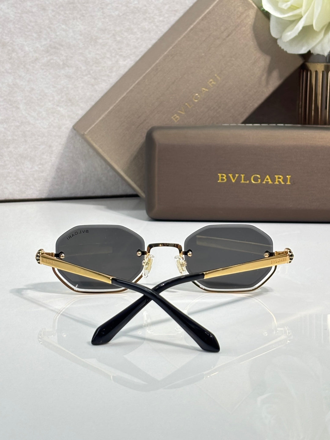 Octagonal sunglasses with gold-tone frame and dark lenses, crossed temple view
