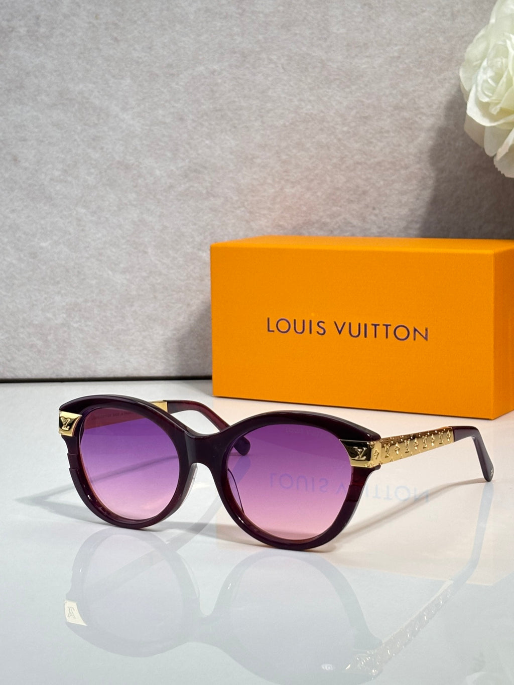 Sunglasses with dark round frames, gold-tone temple detailing, and purple-tinted lenses