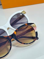 Close-up of sunglasses with white and dark round frames and gold-tone hinges