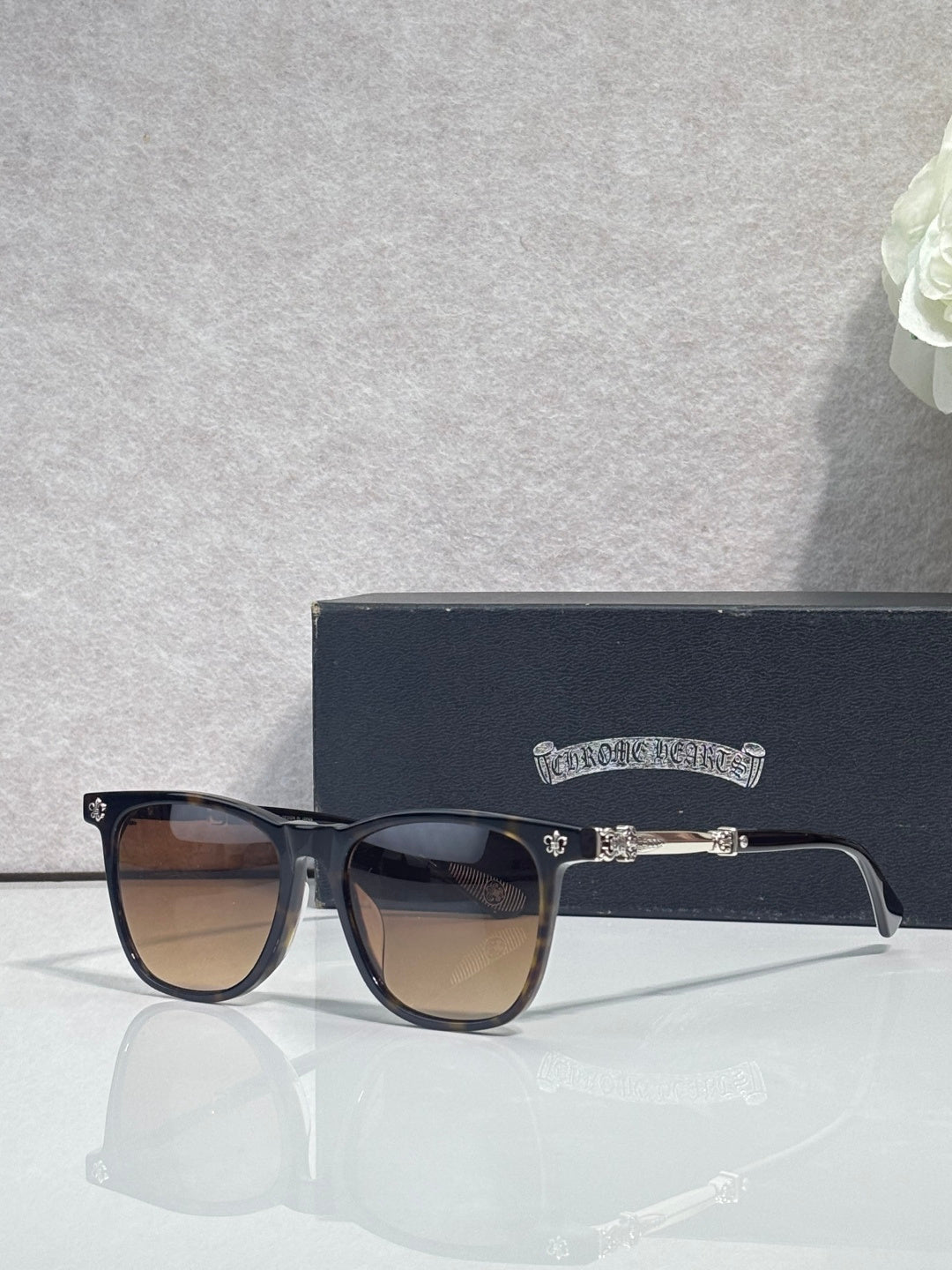 Chrome glasses with dark frames, brown-tinted lenses and small metal emblem on temple