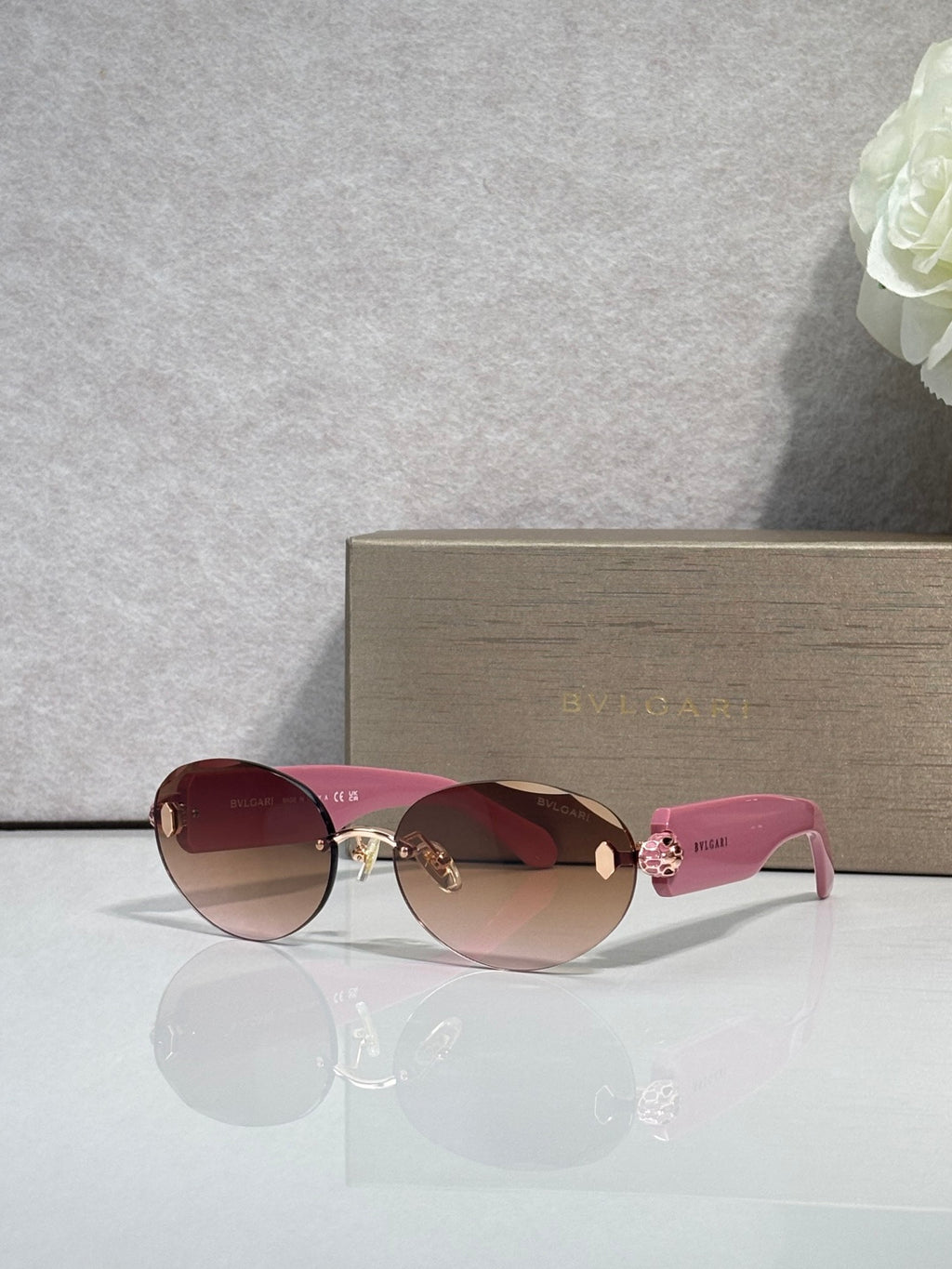 Sunglasses with reddish lenses, pink temples, and gold-tone decorative hardware