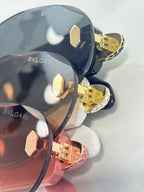 Sunglasses close-up with dark lenses and gold-tone studded hinges in mixed colors