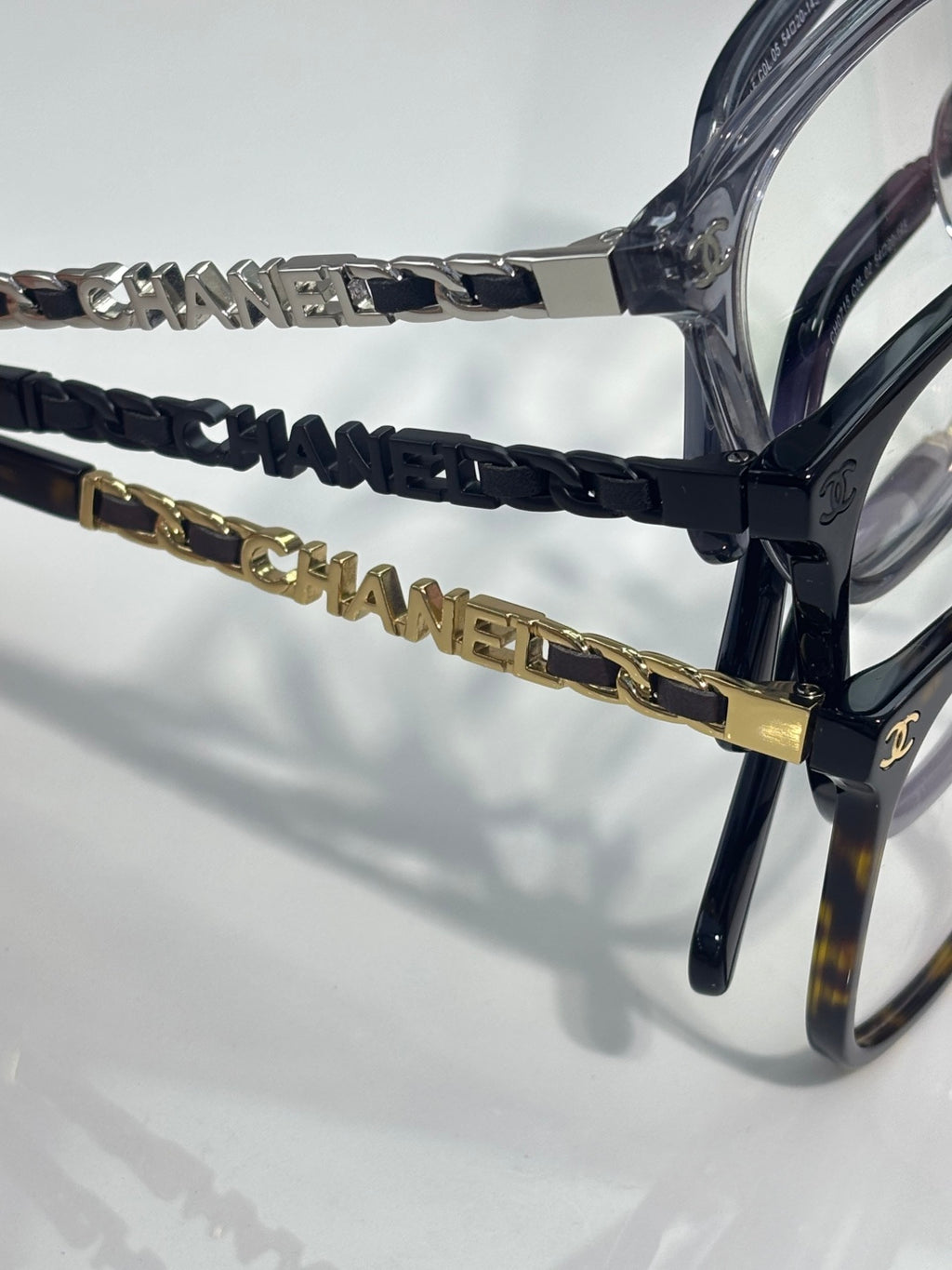 Eyeglasses close-up of dark blue temple chain with gold CHANEL emblem hardware.