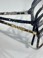 Eyeglasses close-up of dark blue temple chain with gold CHANEL emblem hardware.