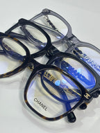 Eyeglasses top view with dark blue frames, blue lenses, and CHANEL branding on arms.