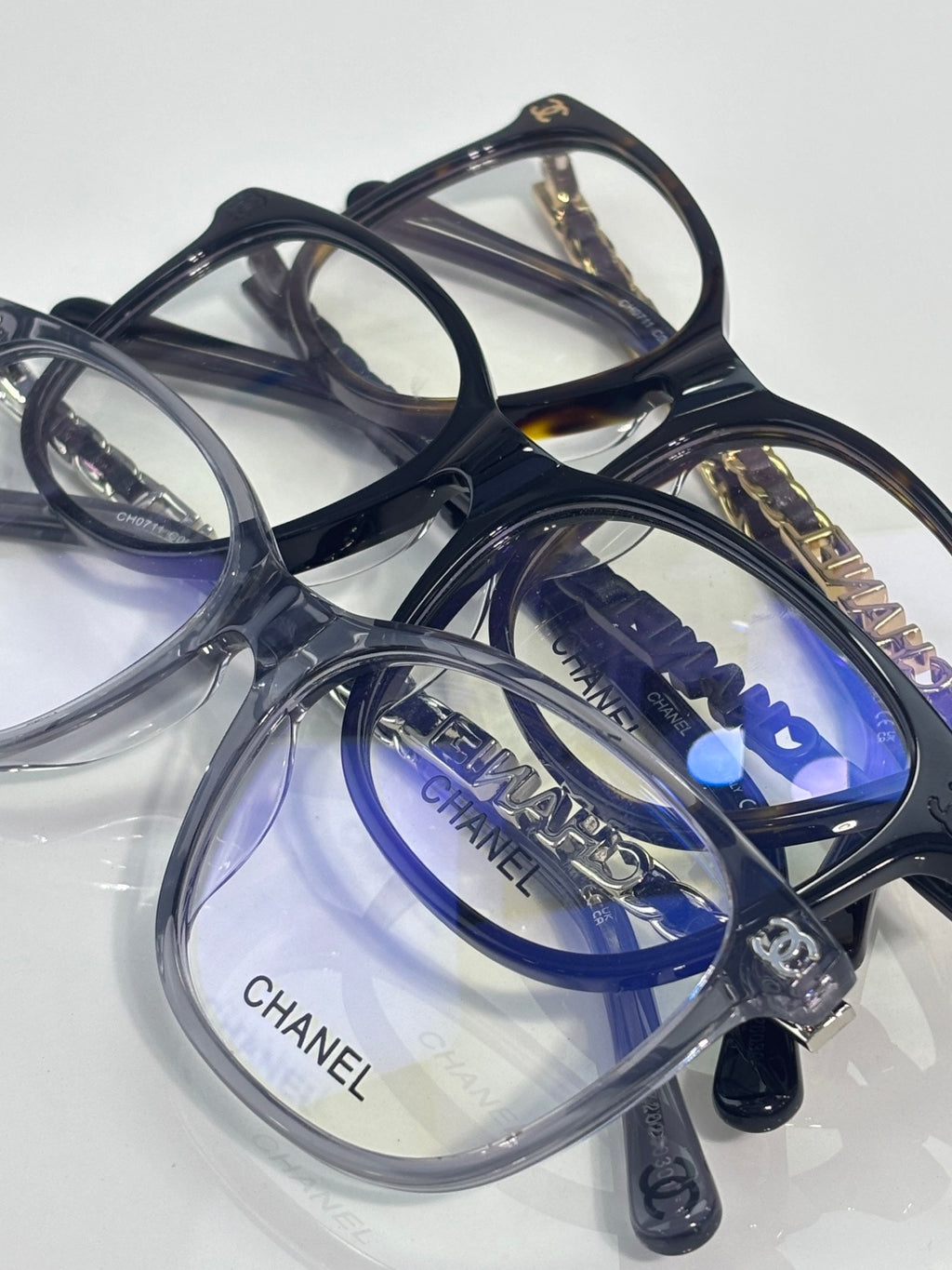 Chanel glasses on clear stand with dark frames and blue-tinted lenses, angled view
