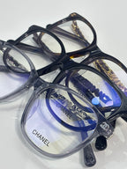 Chanel glasses on clear stand with dark frames and blue-tinted lenses, angled view