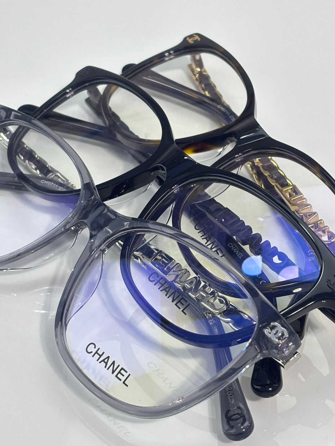 Chanel glasses on clear stand with dark frames and blue-tinted lenses, angled view