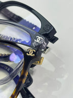 Close-up dark eyeglass frame with Chanel logo at hinge and blue lens tint