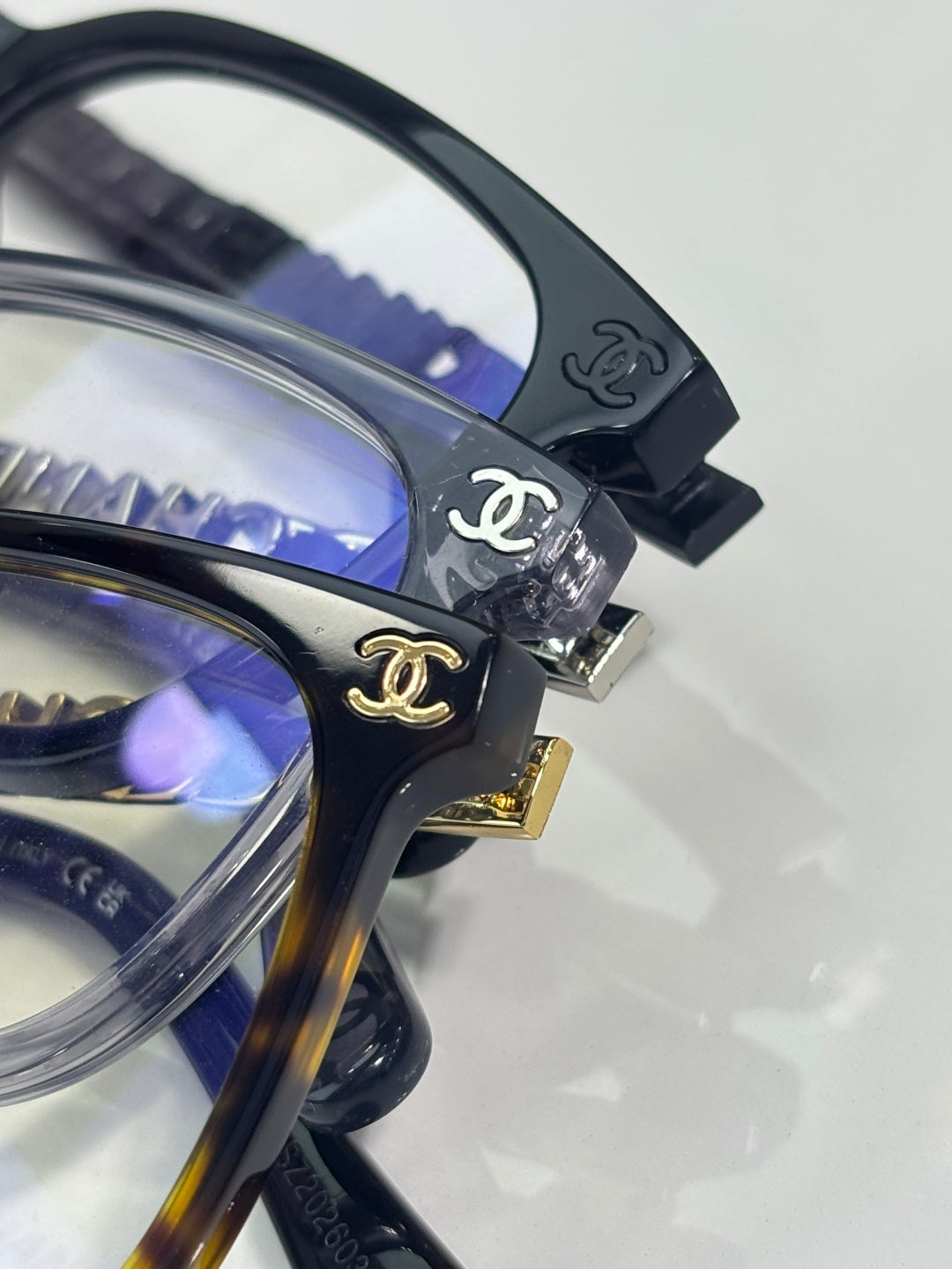 Close-up dark eyeglass frame with Chanel logo at hinge and blue lens tint