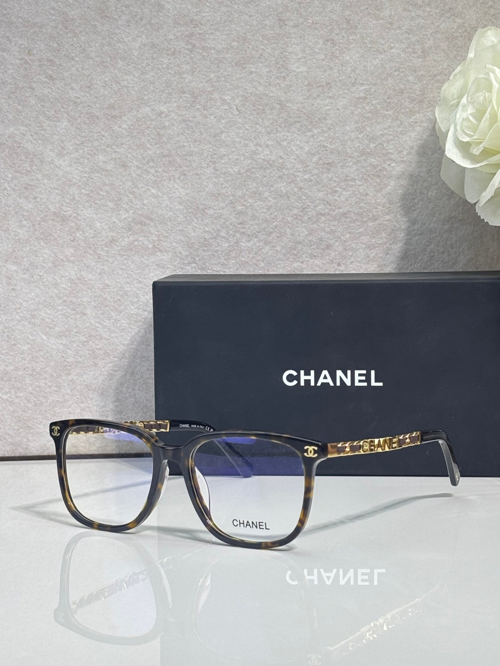 Dark eyeglasses with rectangular frames, blue lenses, gold Chanel logo on temple