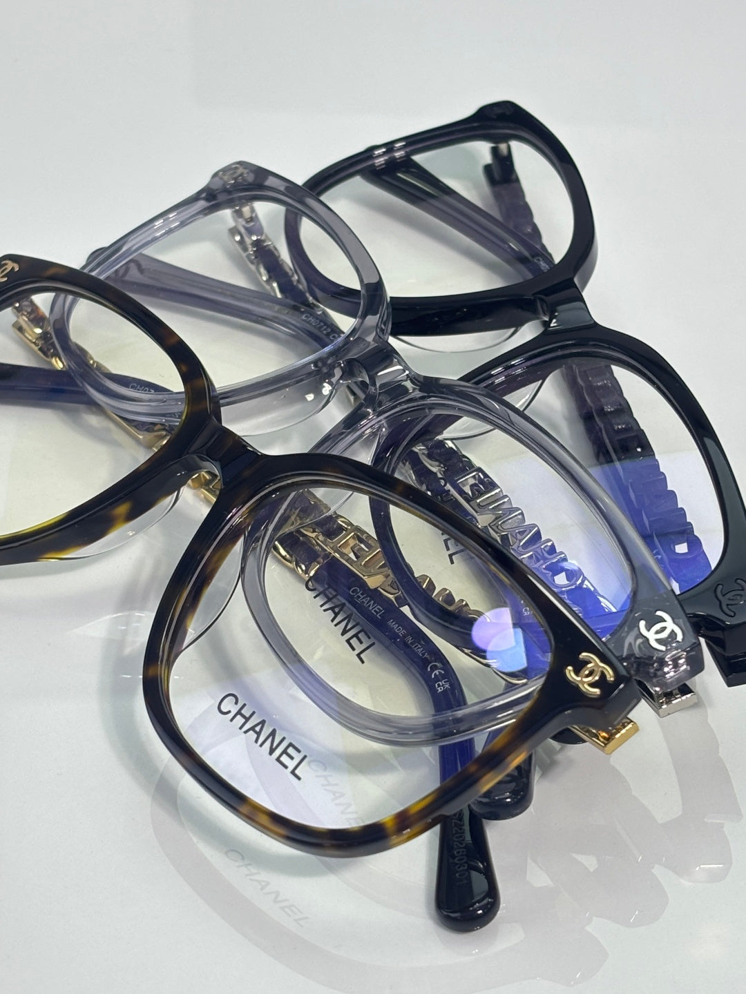 Stacked dark and transparent eyeglasses with blue lenses and gold Chanel logo accents