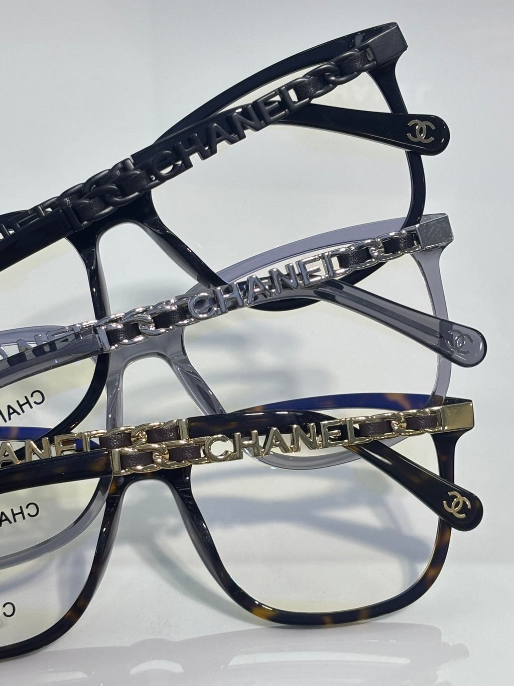 Dark rectangular eyeglasses with chain-linked temple and Chanel logo on frame edge