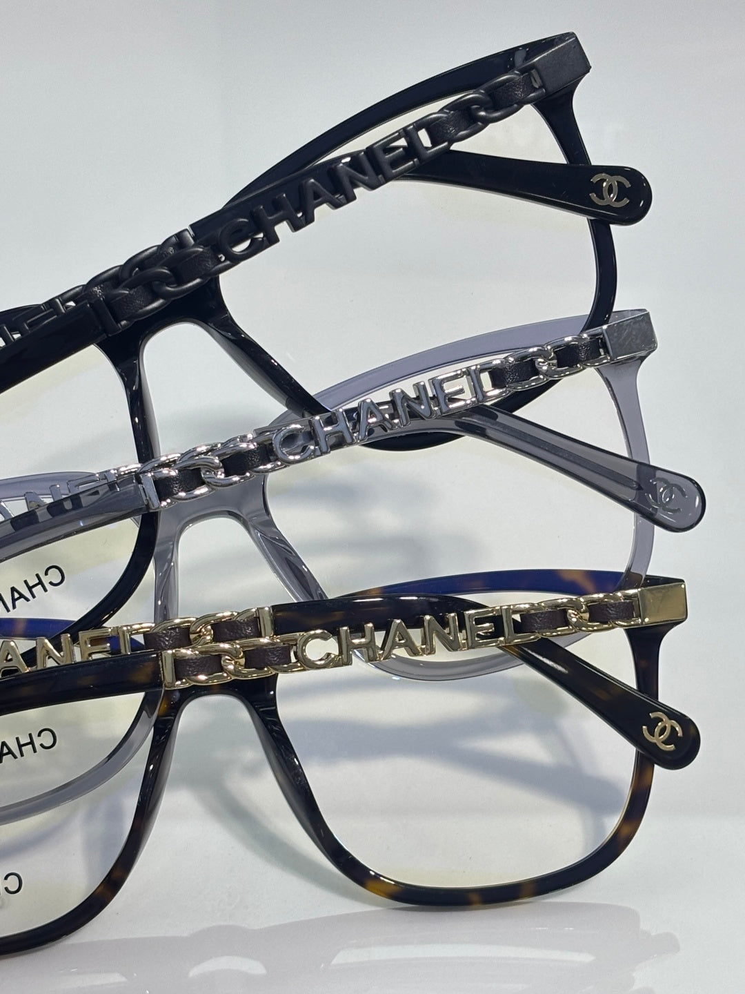 Dark rectangular eyeglasses with chain-linked temple and Chanel logo on frame edge