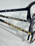 Dark eyeglasses with gold and black chain temple details and Chanel logo hardware