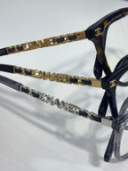 Chanel eyeglass frames close-up, gold chain links and CHANEL lettering on temple