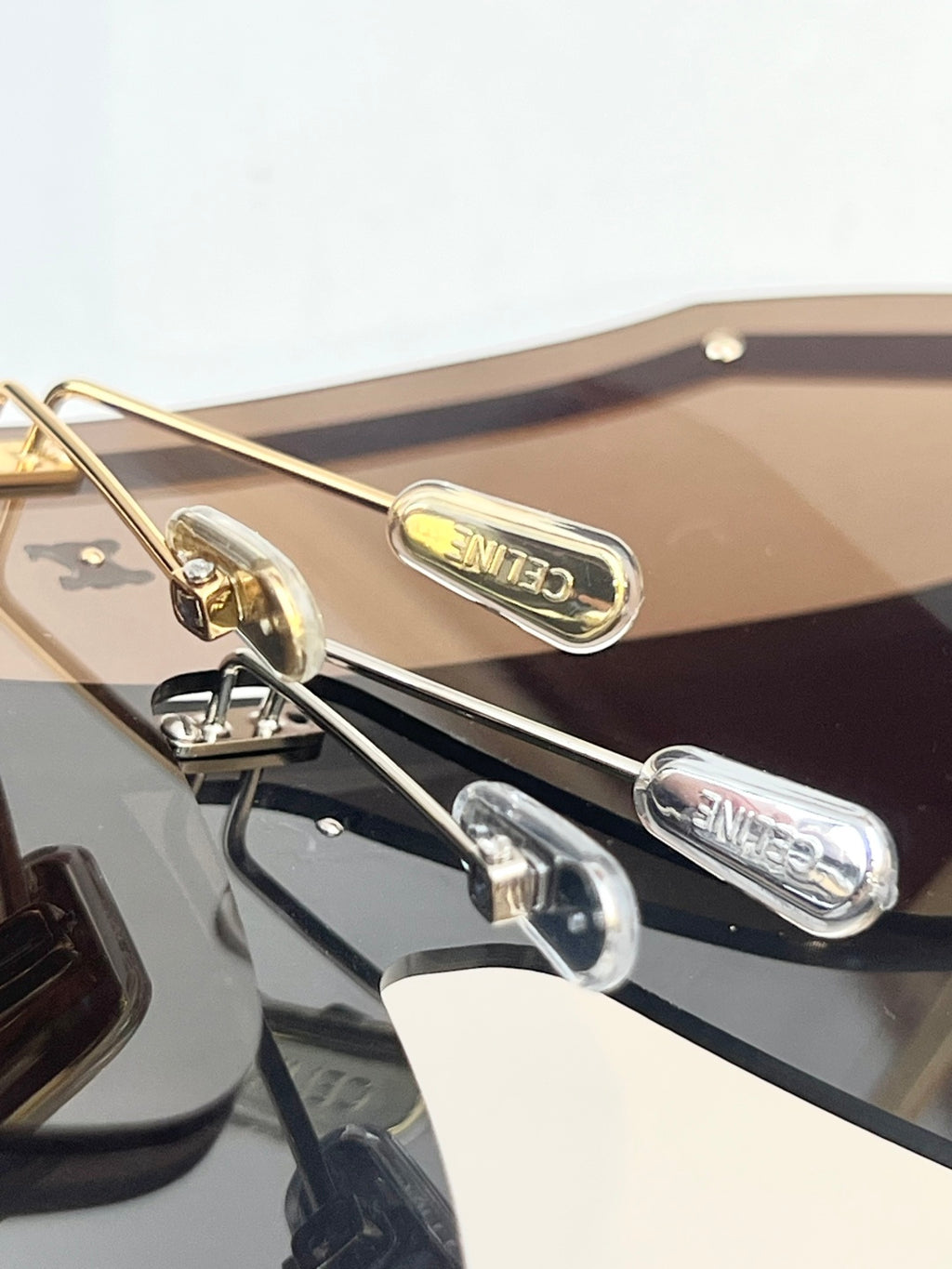 Gold-tone sunglasses hinge detail with tinted lens and engraved accents