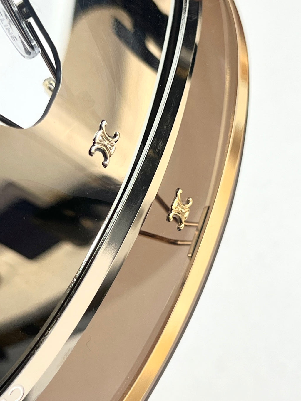 Gold-tone temple detail with decorative emblem and tinted lens edge