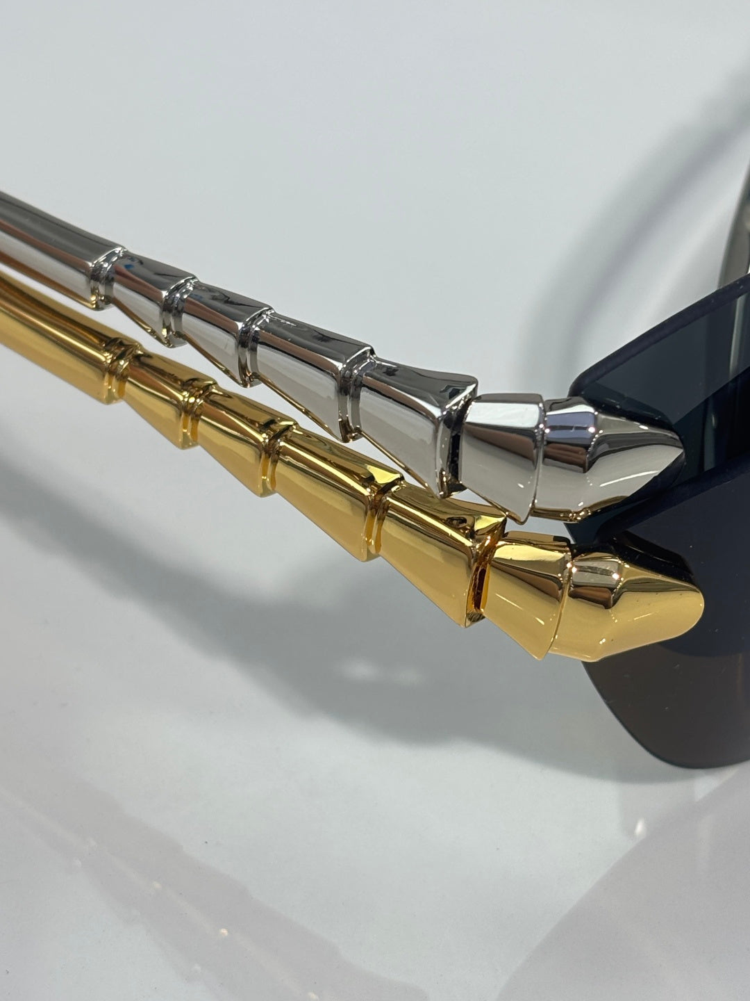 Gold and silver sunglasses temple with metallic hinge detail, close-up.