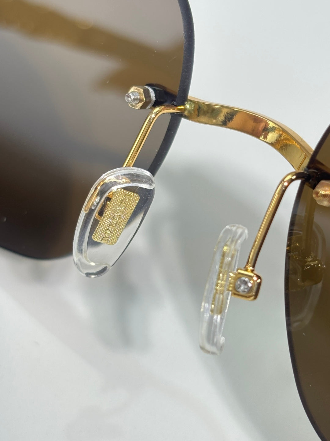 Gold sunglasses temple detail with clear accents and rhinestone logo plate.